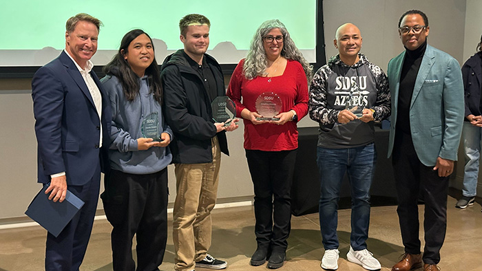 Group photo of the 2024 OneIT Community Award winners at SDSU, holding glass awards and standing with event organizers.