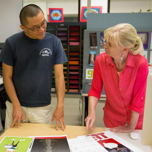 Two graphic designers look over printouts of designs