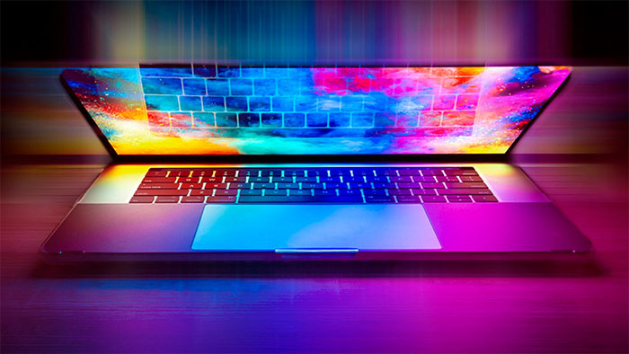 A sleek open laptop with a glowing screen displaying vibrant, multicolored digital patterns that spill over onto the keyboard and surrounding area, creating a futuristic and dynamic lighting effect. (Courtesy of Pixabay)