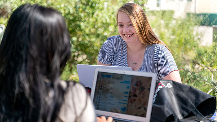 Two SDSU students sitting outside with their laptops.