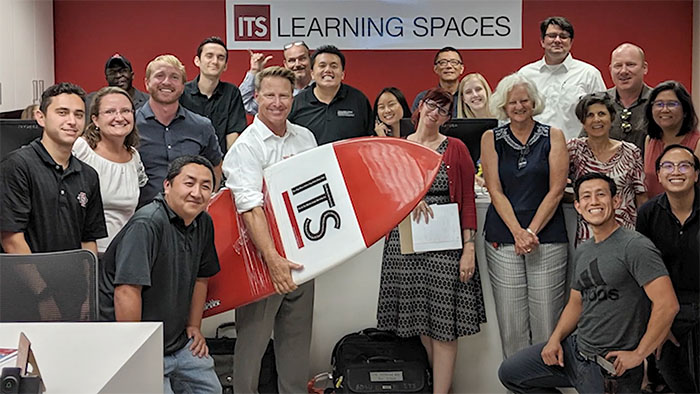 James Frazee holds an ITS surfboard while celebrating with ITS staff and faculty fellows