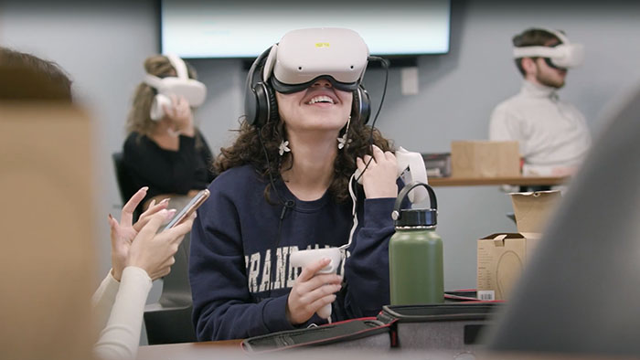A student wearing virtual reality goggles uses hand controls to navigate a VR space