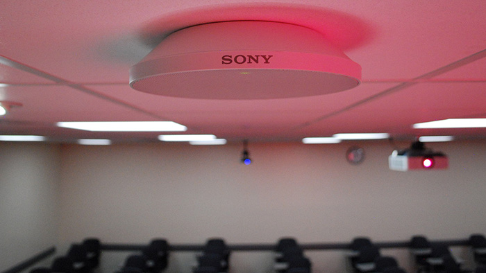 A ceiling-mounted microphone captures the instructor's speech in a classroom