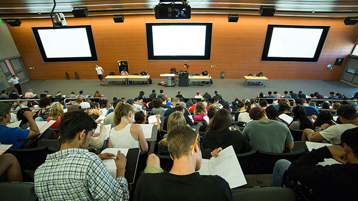 View from the back of large lecture hall of students taking notes